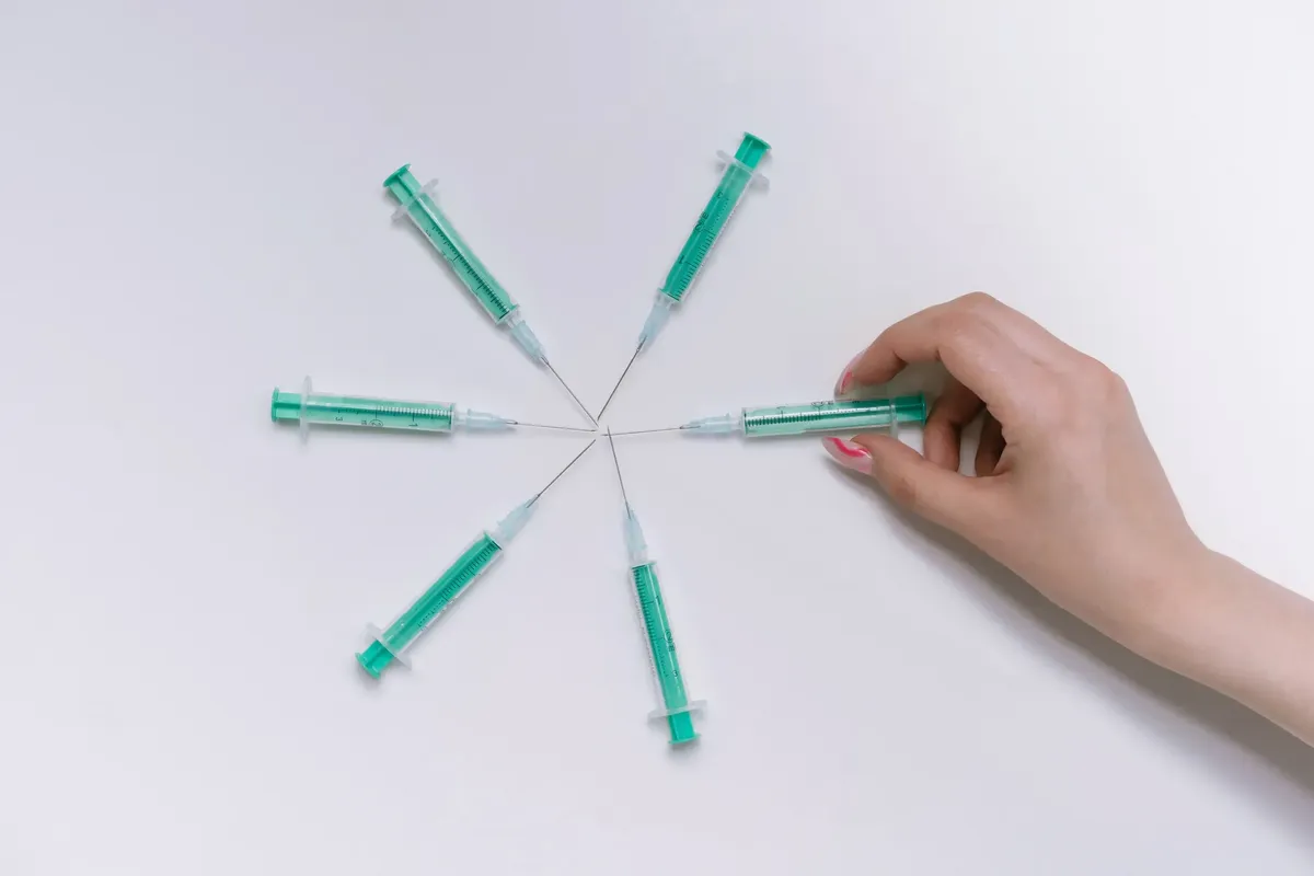 A hand arranges green syringes in a circular pattern on a white surface, symbolizing medical themes.